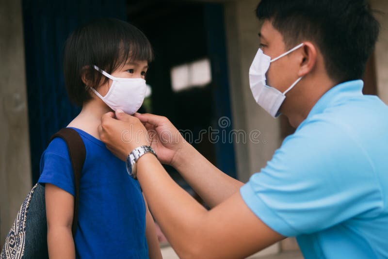 Asian father wearing protective mask puts protective cloth face mask on his little child, schoolkid with backpack is ready to school after Coronavirus COVID-19 pandemic. Asian father wearing protective mask puts protective cloth face mask on his little child, schoolkid with backpack is ready to school after Coronavirus COVID-19 pandemic.