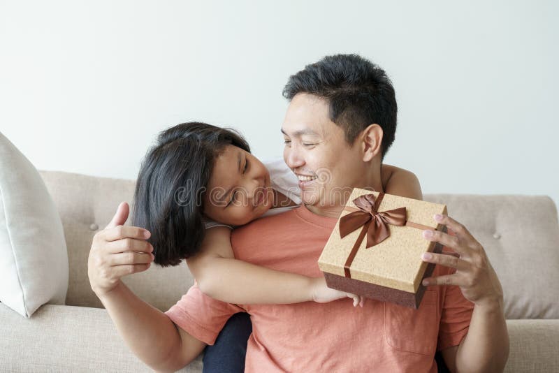 Padre asiático que da a caja de regalo para la hija la sala de estar Muchacha linda y padre que se sientan en el sofá para ser fe fotografía de archivo Padre asiático que da a caja de regalo para la hija la sala de estar Muchacha linda y padre que se sientan en el sofá para ser fe fotografía de archivo