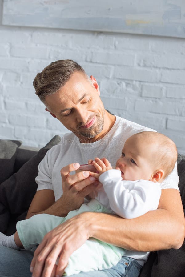 padre bello che si siede sullo strato e sulla figlia d'alimentazione del bambino fotografia stock libera da diritti padre bello che si siede sullo strato e sulla figlia d'alimentazione del bambino fotografia stock libera da diritti