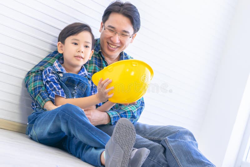 Padre Construtor sentado seu filho segurando capacete de engenheiro para a aprendizagem da carreira familiar e o conceito de educ imagens de stock