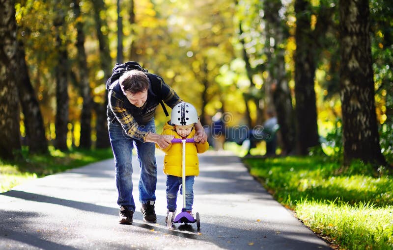 Padre de la Edad Media que muestra a su hijo del niño cómo montar una vespa en un parque del otoño imagen de archivo libre de regalías Padre de la Edad Media que muestra a su hijo del niño cómo montar una vespa en un parque del otoño imagen de archivo libre de regalías