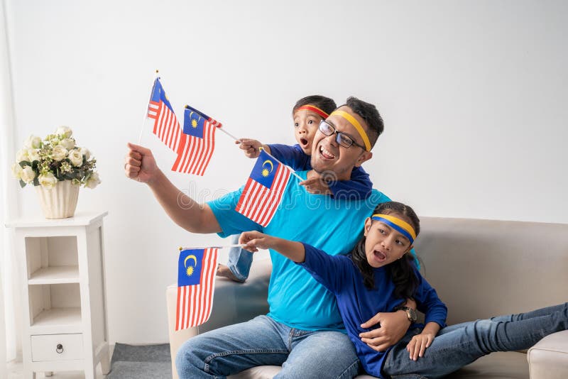 Father and children holding malaysian flag together while watching soccer match at home. Father and children holding malaysian flag together while watching soccer match at home