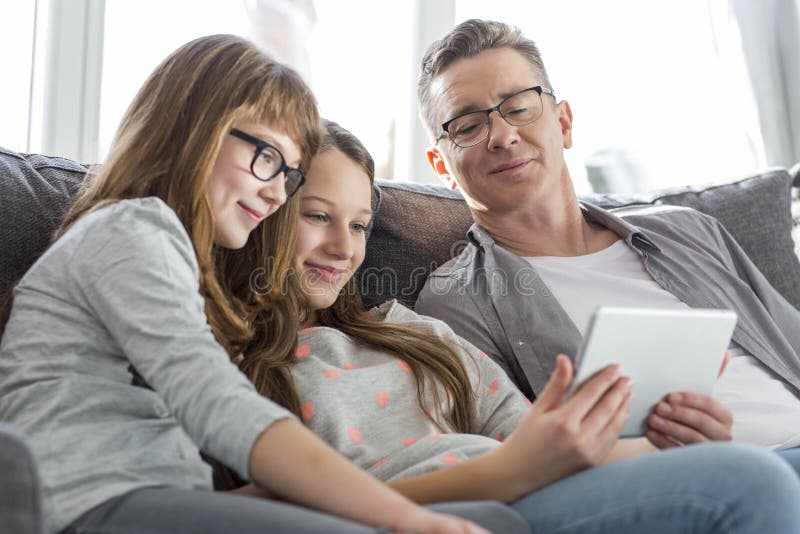Padre e figlie che per mezzo del PC della compressa sul sofà a casa fotografie stock libere da diritti Padre e figlie che per mezzo del PC della compressa sul sofà a casa fotografie stock libere da diritti