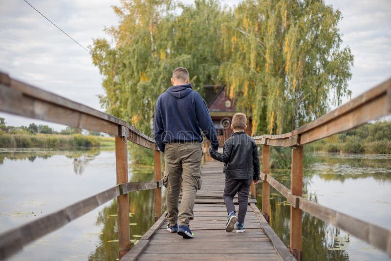 Padre e figlio felici abbracciandosi e giocando insieme in natura verde. casa di pescatori con un ponte pedonale di legno su un mi fotografia stock