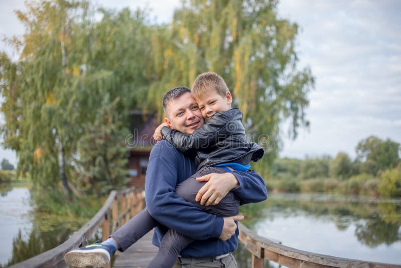 Padre e figlio felici abbracciandosi e giocando insieme in natura verde. casa di pescatori con un ponte pedonale di legno su un mi fotografie stock libere da diritti
