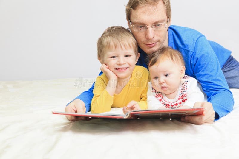 Padre e libro di lettura di due bambini a letto fotografia stock Padre e libro di lettura di due bambini a letto fotografia stock