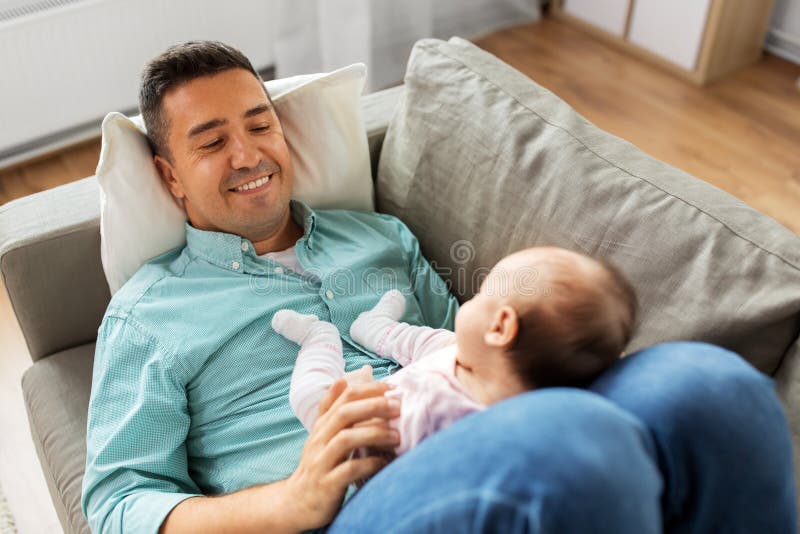 Padre envejecido medio con el bebé que miente en el sofá en casa imágenes de archivo libres de regalías Padre envejecido medio con el bebé que miente en el sofá en casa imágenes de archivo libres de regalías