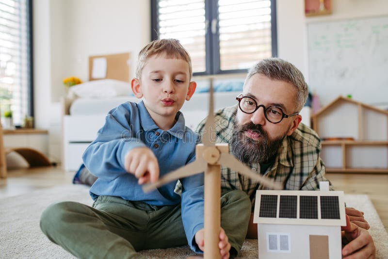 Father explaining renewable green energy, teaching about sustainable lifestyle his young son. Playing with model of house with solar panels, wind turibine at home. Learning through play. Father explaining renewable green energy, teaching about sustainable lifestyle his young son. Playing with model of house with solar panels, wind turibine at home. Learning through play.