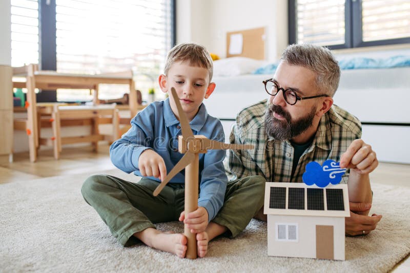 Father explaining renewable green energy, teaching about sustainable lifestyle his young son. Playing with model of house with solar panels, wind turibine at home. Learning through play. Father explaining renewable green energy, teaching about sustainable lifestyle his young son. Playing with model of house with solar panels, wind turibine at home. Learning through play.