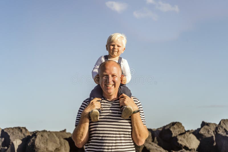 Padre felice che tiene il suo piccolo figlio biondo sulla sua spalla fotografia stock
