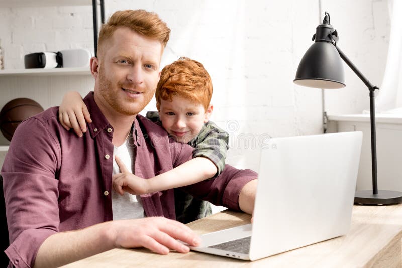 Padre feliz e hijo que sonríen en la cámara mientras que usando el ordenador portátil junto imagen de archivo libre de regalías