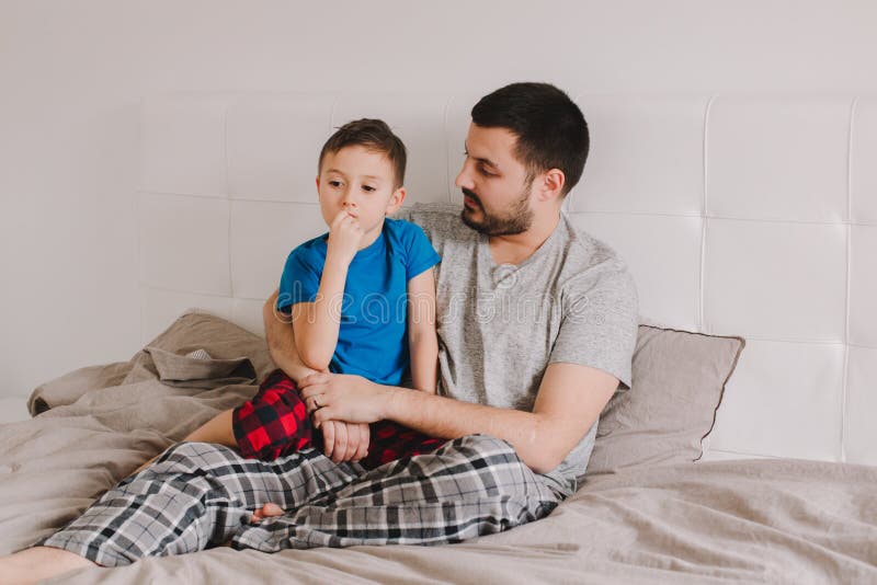 Padre joven caucásico hablando con su hijo Hombre padre abrazando con un niño en la cama en la habitación de su casa Auténtico es fotografía de archivo libre de regalías Padre joven caucásico hablando con su hijo Hombre padre abrazando con un niño en la cama en la habitación de su casa Auténtico es fotografía de archivo libre de regalías
