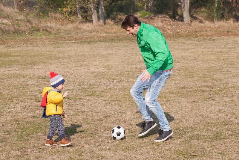 Padre joven con su pequeño hijo que juega al fútbol, fútbol en el parque foto de archivo libre de regalías Padre joven con su pequeño hijo que juega al fútbol, fútbol en el parque foto de archivo libre de regalías