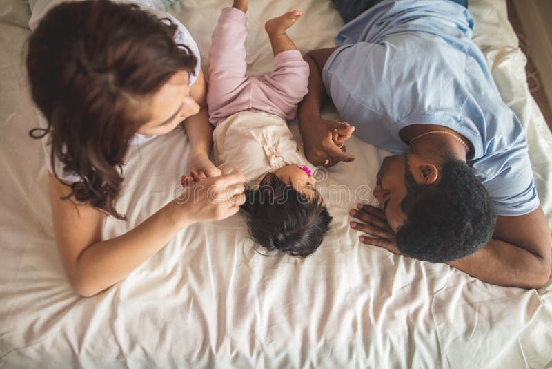 Padre joven feliz, madre y bebé lindo mintiendo en la cama fotos de archivo libres de regalías Padre joven feliz, madre y bebé lindo mintiendo en la cama fotos de archivo libres de regalías