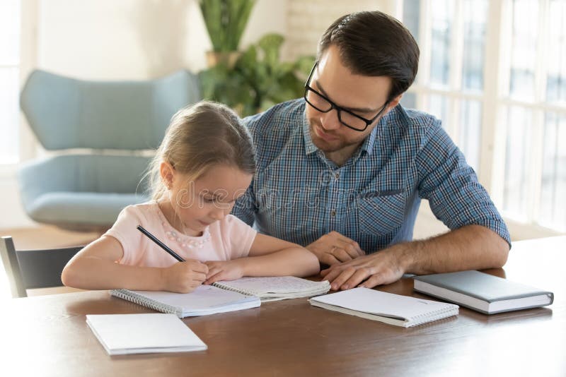 Padre joven que cuida a la pequeña hija con los deberes. imágenes de archivo libres de regalías