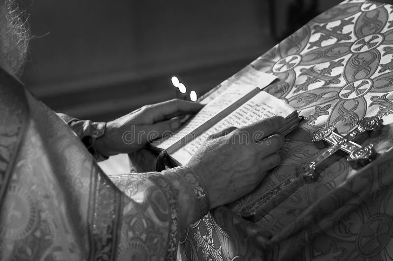 Padre preto e branco que reza na igreja que guarda a Bíblia e a cruz do azevinho com velas fotografia de stock Padre preto e branco que reza na igreja que guarda a Bíblia e a cruz do azevinho com velas fotografia de stock