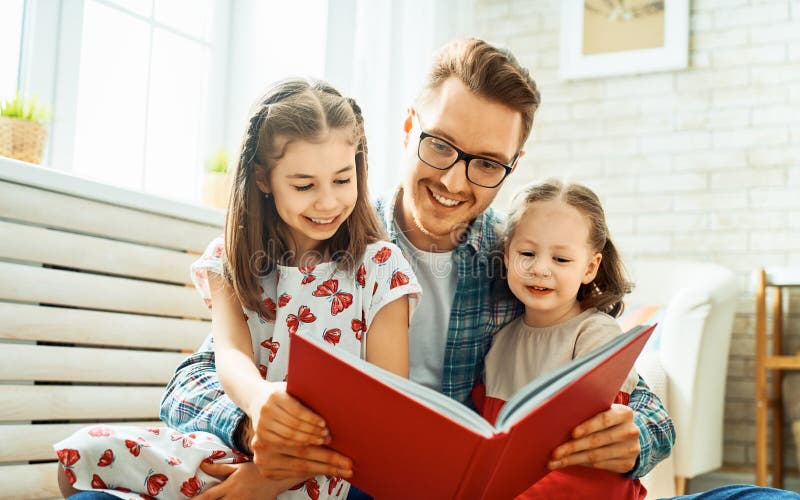 Padre que lee un libro a sus hijas imágenes de archivo libres de regalías Padre que lee un libro a sus hijas imágenes de archivo libres de regalías
