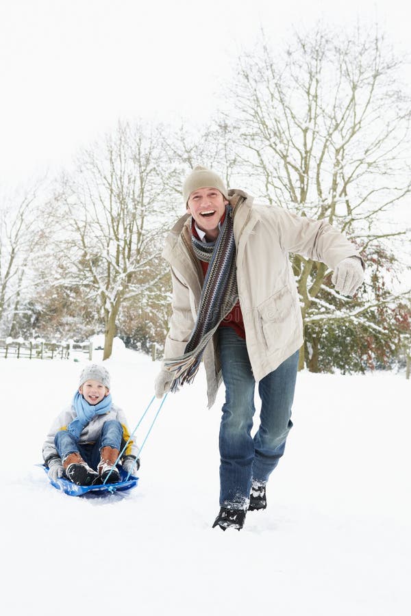 Padre que tira del hijo en el trineo a través de nieve fotos de archivo Padre que tira del hijo en el trineo a través de nieve fotos de archivo