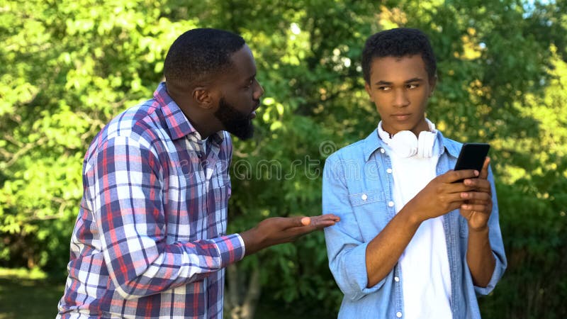 Padre regañando a hijo adolescente macho jugando un juego de smartphones ignorando la educación de sus padres foto de archivo Padre regañando a hijo adolescente macho jugando un juego de smartphones ignorando la educación de sus padres foto de archivo