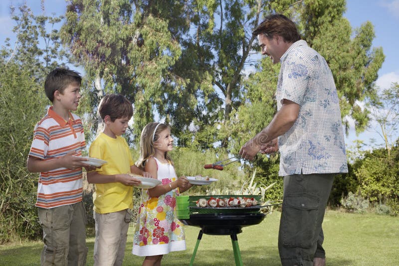 Padre Serving Grilled Food a los niños al aire libre fotos de archivo libres de regalías Padre Serving Grilled Food a los niños al aire libre fotos de archivo libres de regalías