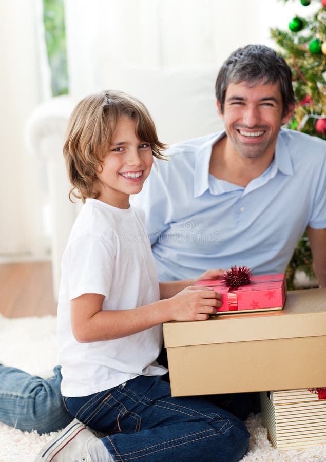 Padre sonriente y sus regalos de la Navidad de la apertura del hijo imágenes de archivo libres de regalías Padre sonriente y sus regalos de la Navidad de la apertura del hijo imágenes de archivo libres de regalías