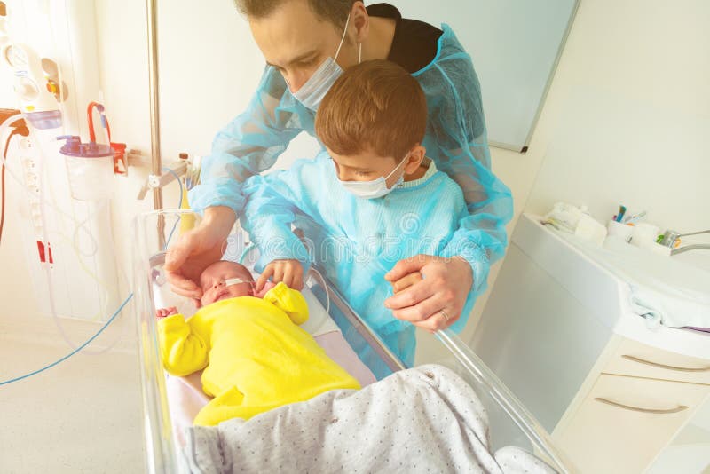 Father with little boy brother near premature born infant crib in ICU in hospital room. Father with little boy brother near premature born infant crib in ICU in hospital room