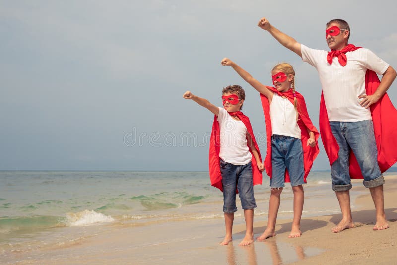 Padre y niños que juegan al super héroe en la playa en el ti del día imagen de archivo Padre y niños que juegan al super héroe en la playa en el ti del día imagen de archivo