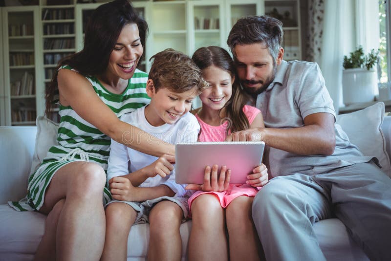 Padres que se sientan en el sofá con sus niños y que usan la tableta digital en sala de estar