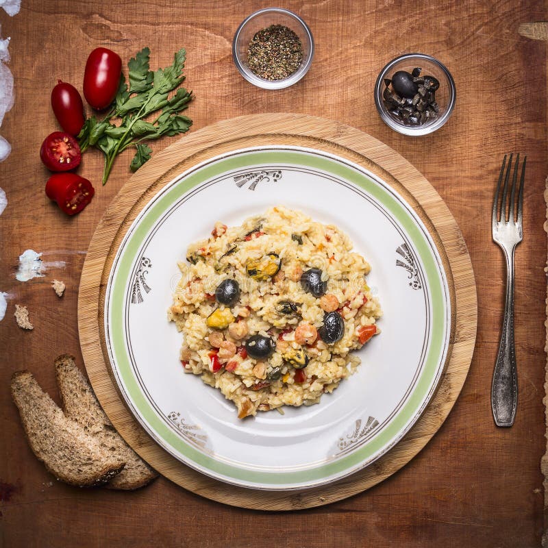 Paella cozinhado com prato do marisco em uma placa de desbastamento com o pão temperado com ervas e tomates uma forquilha no back imagens de stock royalty free Paella cozinhado com prato do marisco em uma placa de desbastamento com o pão temperado com ervas e tomates uma forquilha no back imagens de stock royalty free