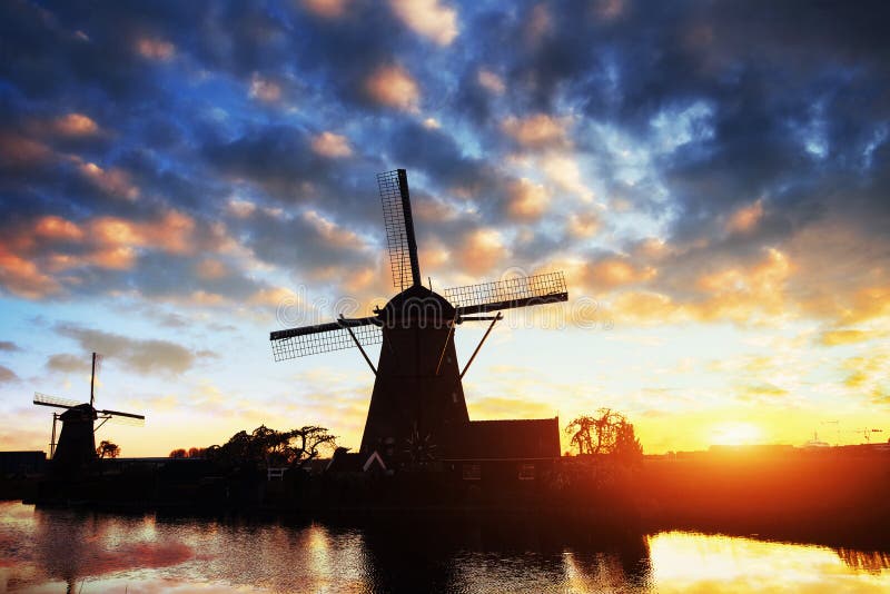 Paesaggio con il bello mulino olandese tradizionale vicino ai corsi di acqua con il tramonto e la riflessione fantastici in acqua immagini stock libere da diritti Paesaggio con il bello mulino olandese tradizionale vicino ai corsi di acqua con il tramonto e la riflessione fantastici in acqua immagini stock libere da diritti