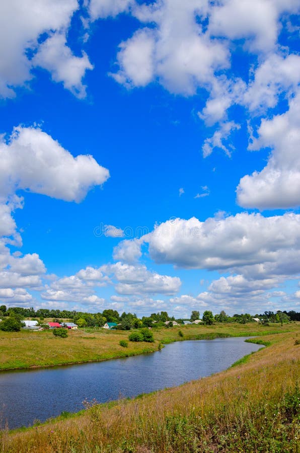 Paesaggio soleggiato di estate con il fiume, i campi dell'azienda agricola, le colline verdi e le belle nuvole in cielo blu immagini stock Paesaggio soleggiato di estate con il fiume, i campi dell'azienda agricola, le colline verdi e le belle nuvole in cielo blu immagini stock