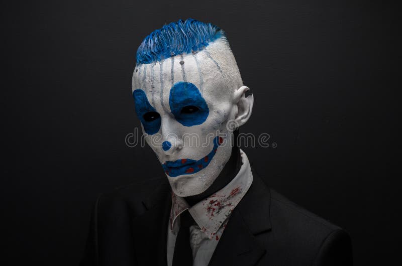 Pagliaccio terribile e tema di Halloween: Pagliaccio blu pazzo in vestito nero isolato su un fondo scuro nello studio immagini stock libere da diritti Pagliaccio terribile e tema di Halloween: Pagliaccio blu pazzo in vestito nero isolato su un fondo scuro nello studio immagini stock libere da diritti