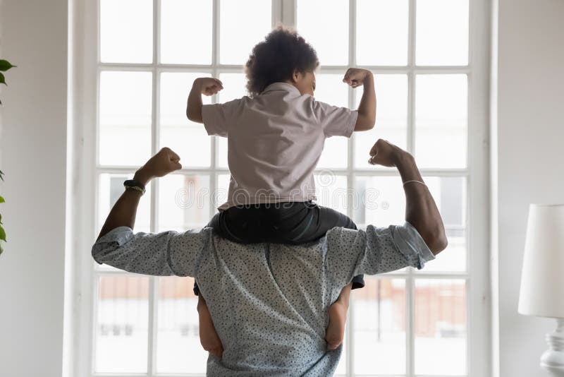 Pai americano africano com filho pequeno em ombros mostrando bíceps.