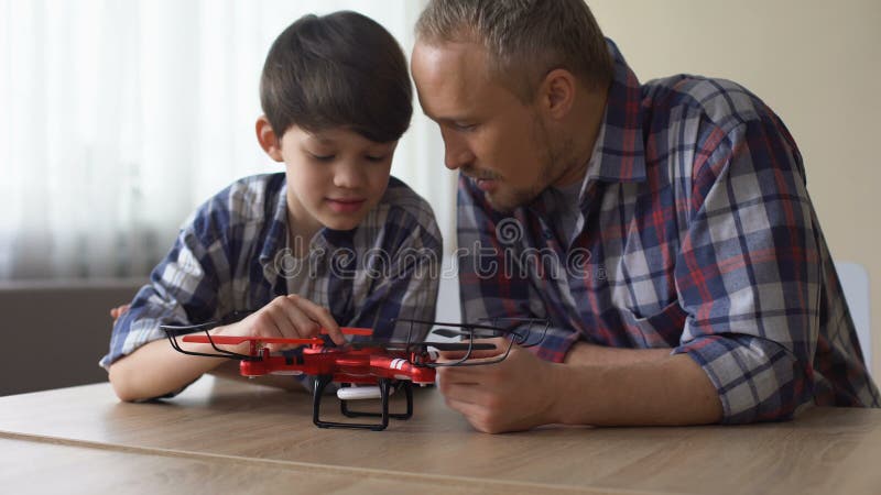 Pai curioso e filho pequeno que examinam o modelo novo do quadrocopter em casa, divertimento