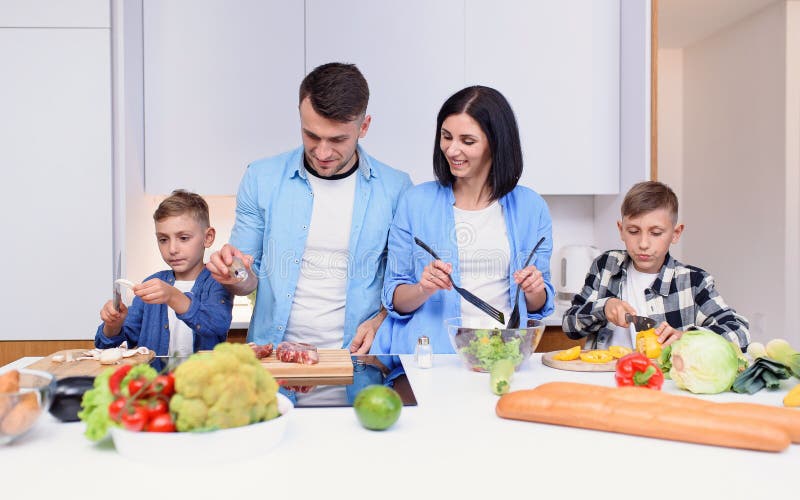 Família jovem e elegante com dois filhos preparando um café da manhã  vegetariano saudável com legumes frescos na cozinha