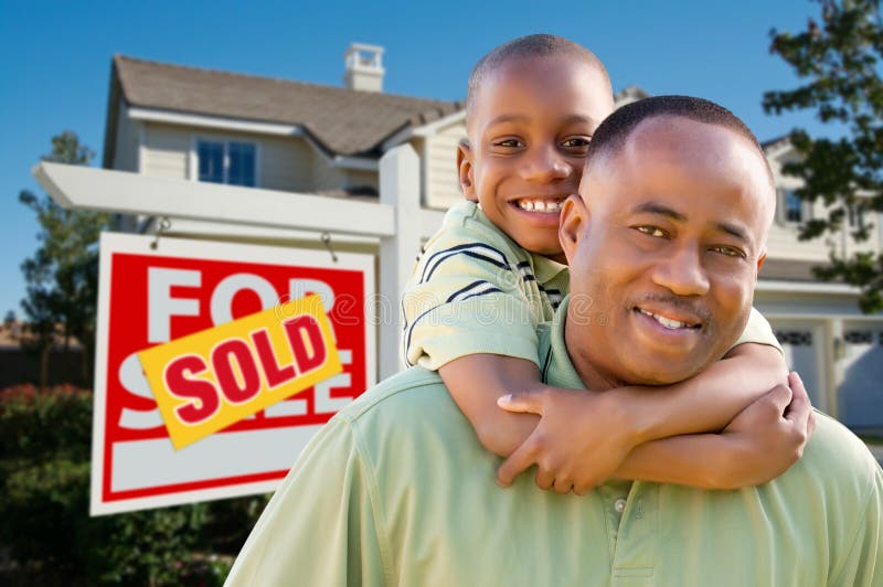 Happy African American Father and Son in Front of New Home and Sold Real Estate Sign. Happy African American Father and Son in Front of New Home and Sold Real Estate Sign.