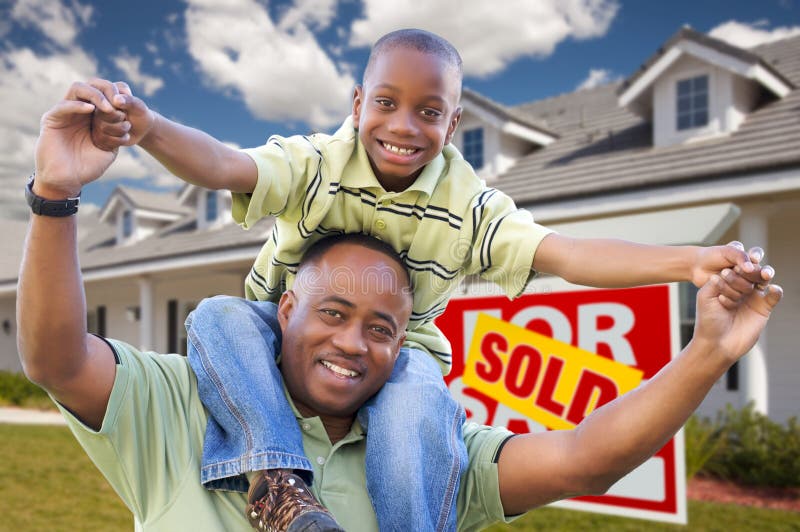 Happy African American Father and Son in Front of New Home and Sold Real Estate Sign. Happy African American Father and Son in Front of New Home and Sold Real Estate Sign.