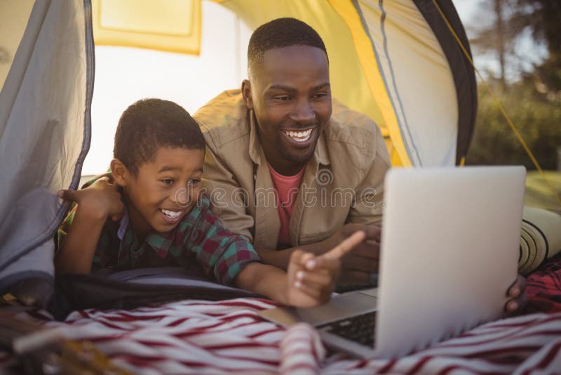Pai e filho de sorriso que usa o portátil na barraca imagem de stock Pai e filho de sorriso que usa o portátil na barraca imagem de stock