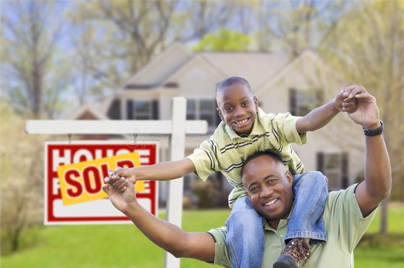 Happy African American Father and Son in Front of New Home and Sold Real Estate Sign. Happy African American Father and Son in Front of New Home and Sold Real Estate Sign.