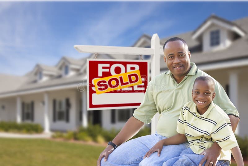 African American Father and Son In Front of Sold For Sale Real Estate Sign and New House. African American Father and Son In Front of Sold For Sale Real Estate Sign and New House.