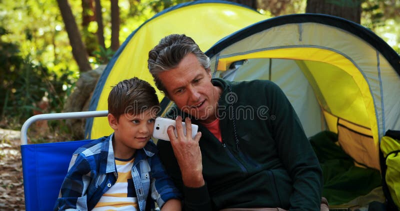 Pai e filho que usa o telefone celular fora da barraca