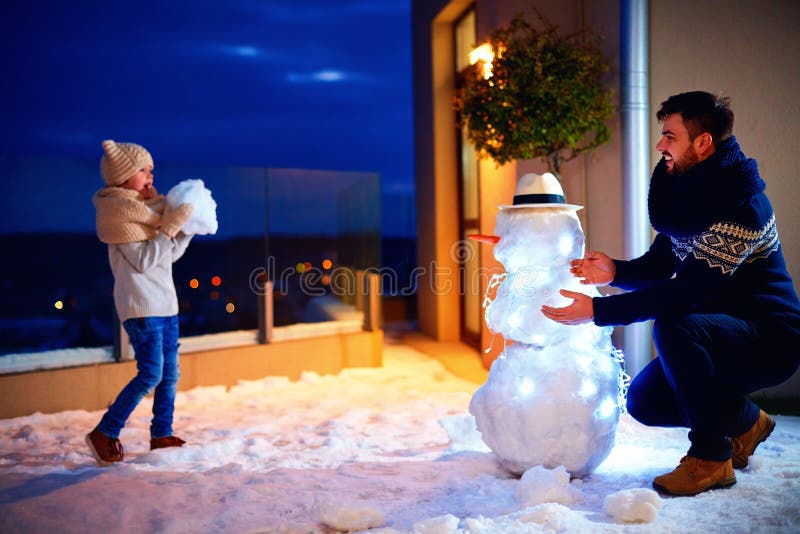 Pai feliz e filho que fazem o boneco de neve na luz da noite foto de stock royalty free