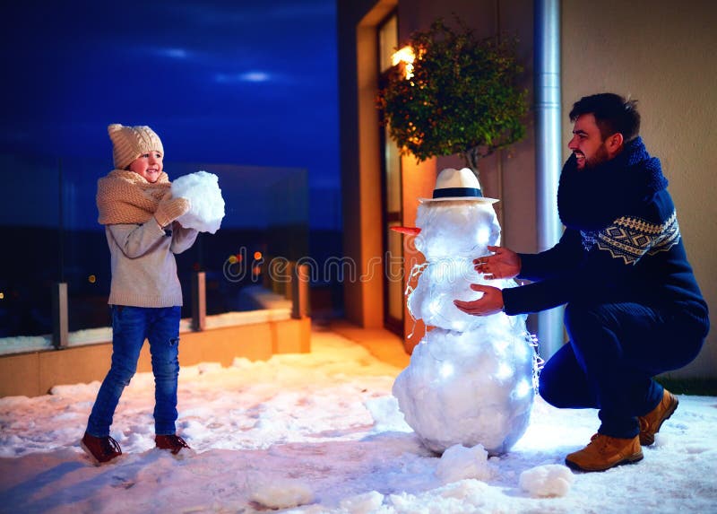 Pai feliz e filho que fazem o boneco de neve na luz da noite imagem de stock