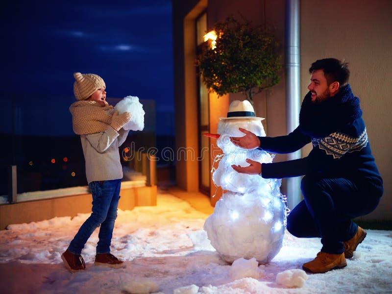 Pai feliz e filho que fazem o boneco de neve na luz da noite fotografia de stock royalty free