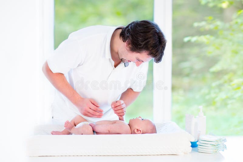 Young happy father playing with his newborn baby son while changing a diaper. Young happy father playing with his newborn baby son while changing a diaper