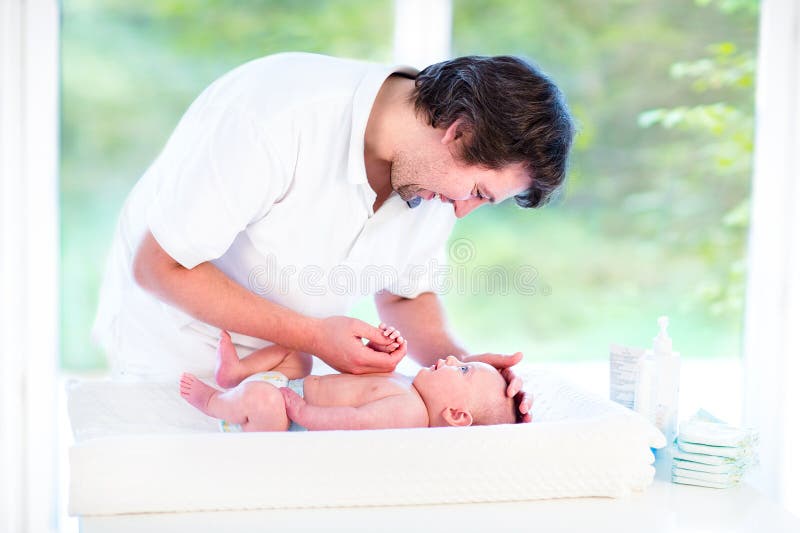 Young happy father playing with his newborn baby son while changing a diaper. Young happy father playing with his newborn baby son while changing a diaper