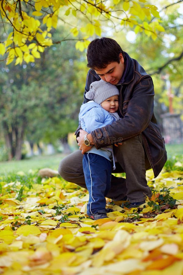 Pai feliz que abraça o filho pequeno no parque do outono fotografia de stock Pai feliz que abraça o filho pequeno no parque do outono fotografia de stock