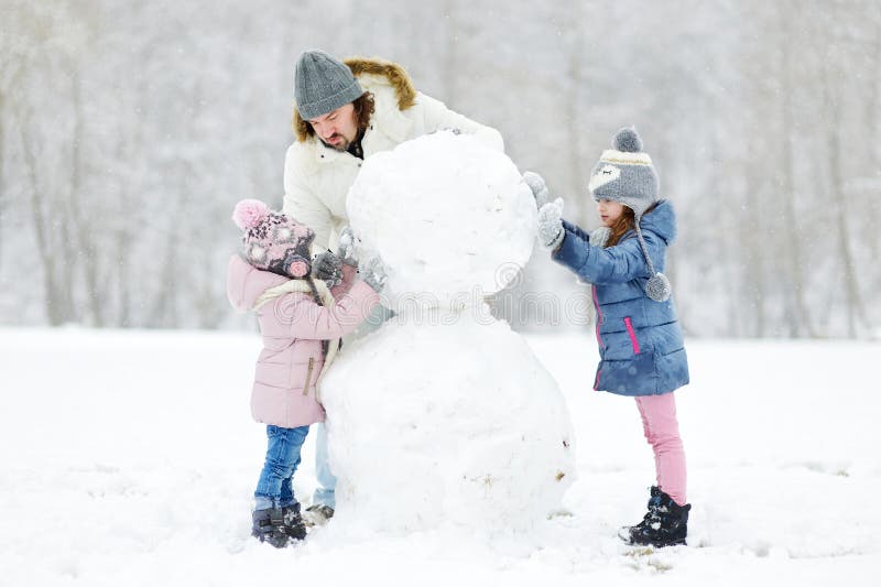 Pai novo e suas filhas que constroem um boneco de neve foto de stock royalty free