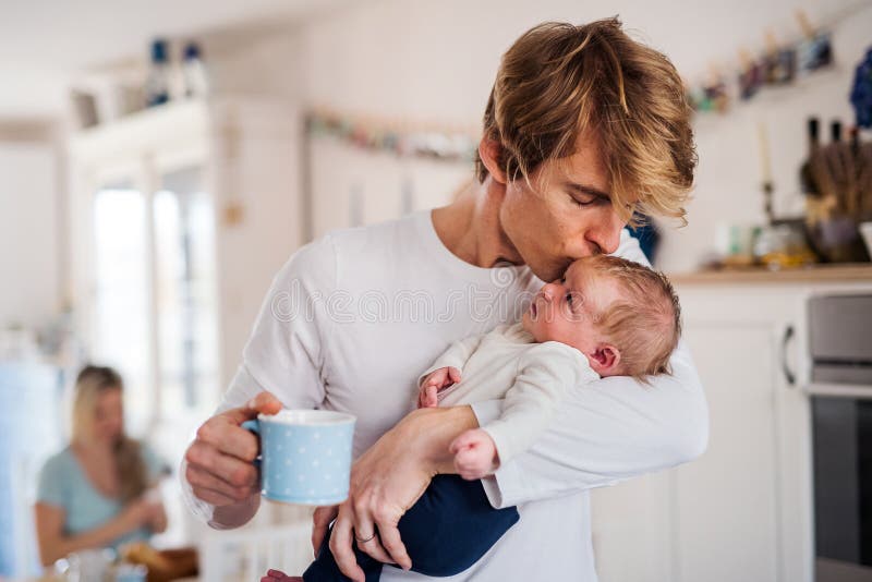Pai novo que guarda um bebê recém-nascido na cozinha em casa, beijando fotos de stock Pai novo que guarda um bebê recém-nascido na cozinha em casa, beijando fotos de stock