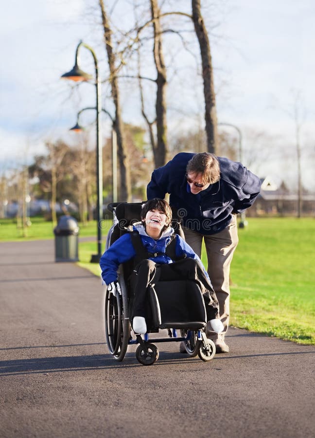 Pai a caminhar com o filho deficiente em cadeira de rodas fotografia de stock royalty free
